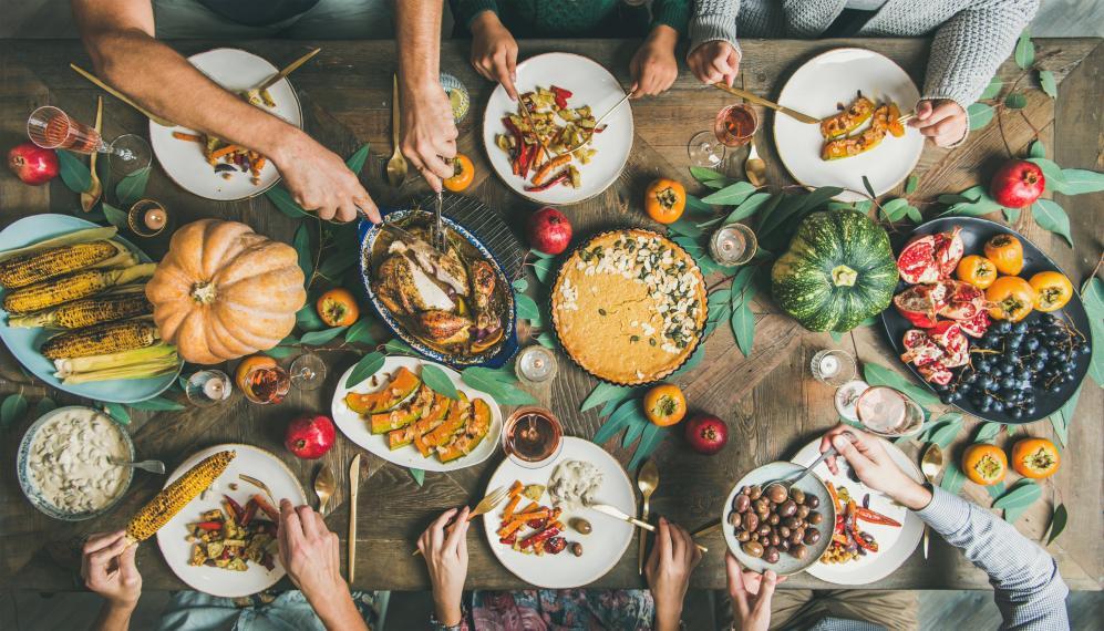 Looking down at a harvest table, with many friends' hands reaching for food