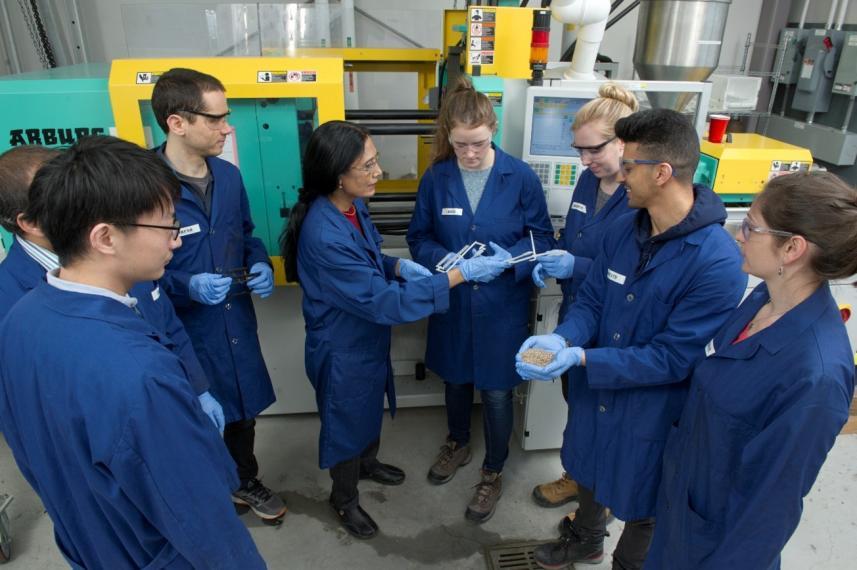 Researchers, all in blue labcoats, gather around Dr. Misra in the lab