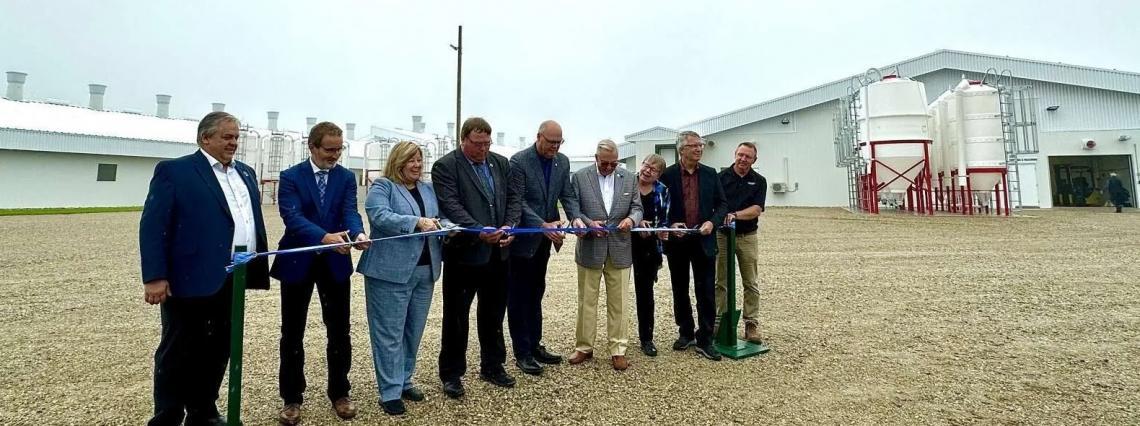 A line of officials in suits cut a ribbon in front of the modern white barns of the Ontario Swine Research Centre