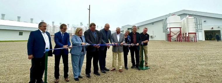 A line of officials in suits cut a ribbon in front of the modern white barns of the Ontario Swine Research Centre