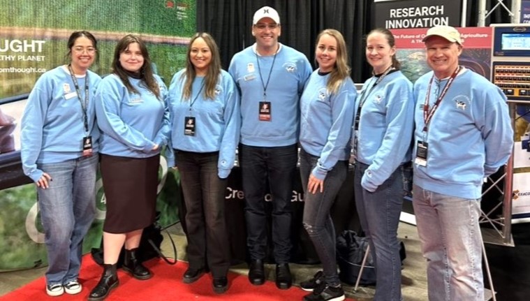 The seven-person group stands together in matching blue shirts, smiling