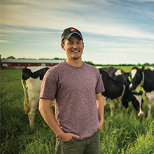 Andrew Campbell standing in a field with Holstein cows behind him.