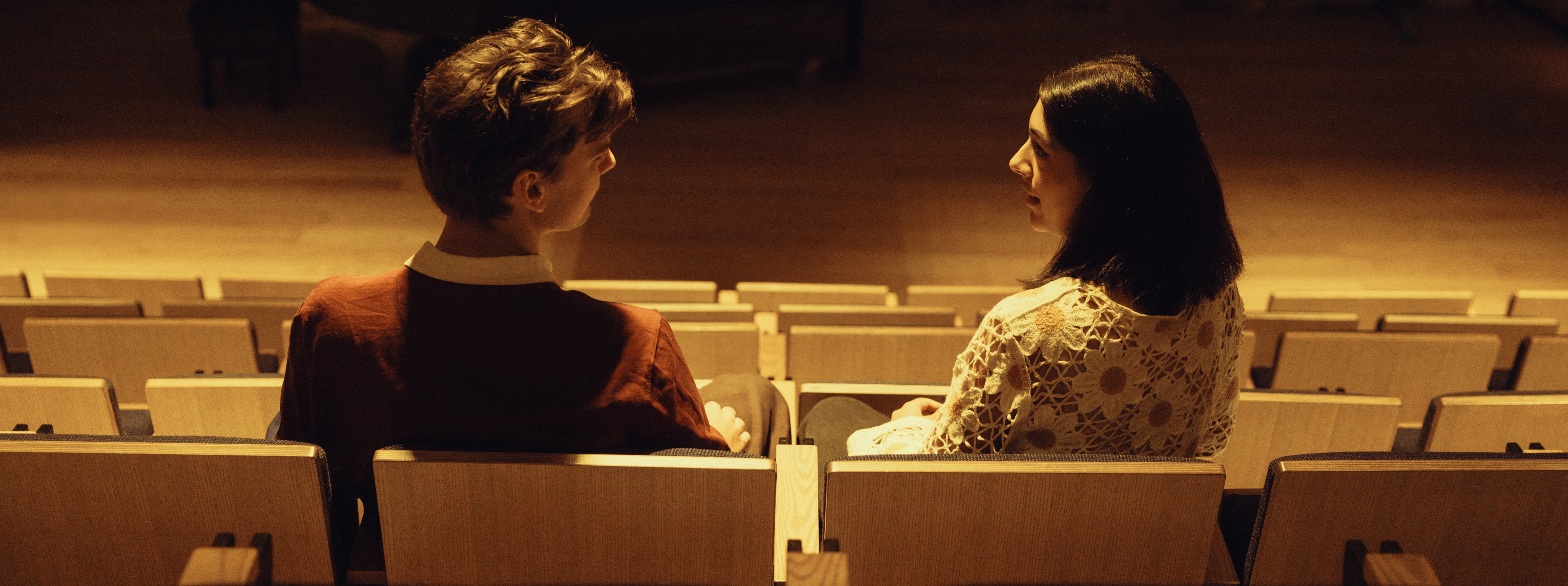 Two students sitting and looking at eachother in auditorium seats.