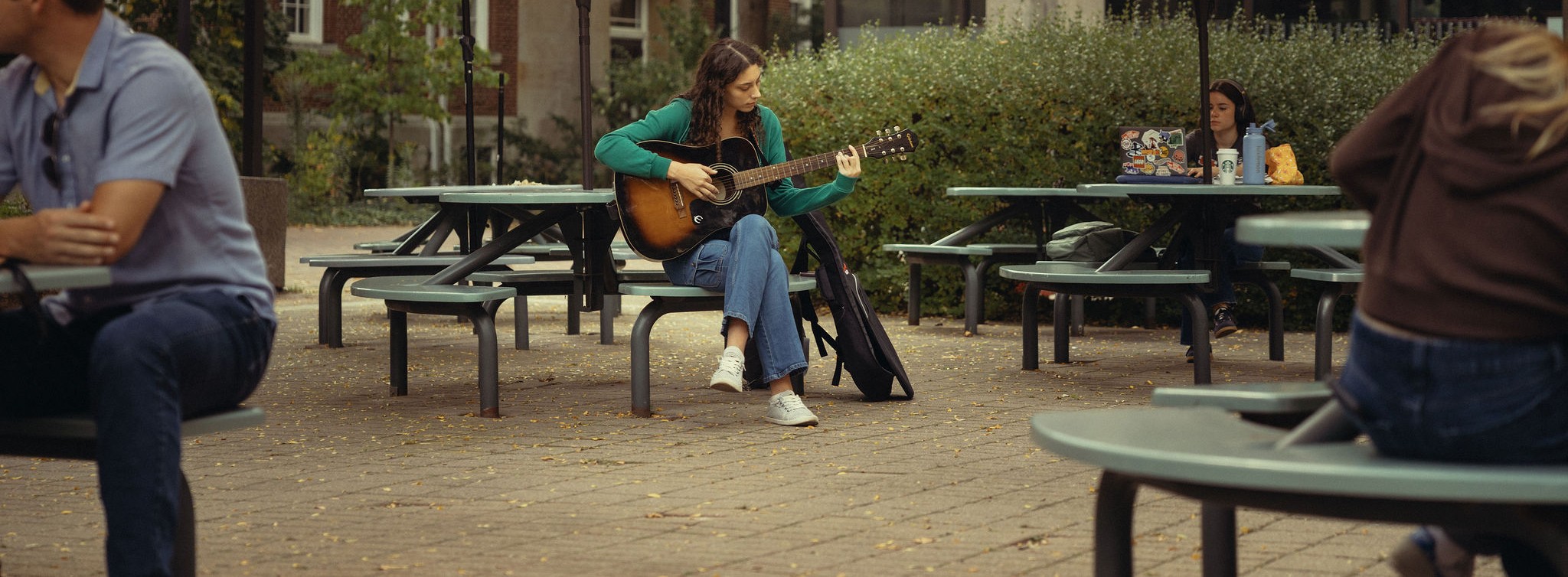 Student sitting at a picnic table playing guitar