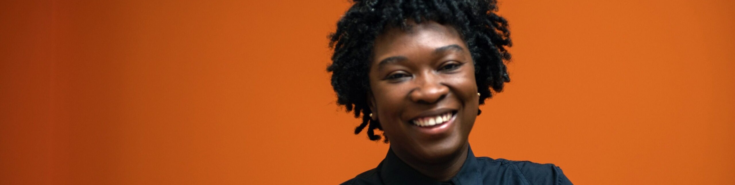 Headshot of Professor Canisia Lubrin smiling in front of an orange background.