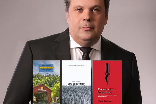 Author Shane Neilson, in a suit, with the covers of his three most recent books.