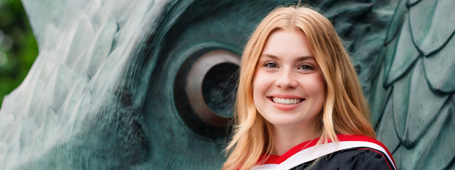 Mya Trombley, Alumnus of the undergraduate History program in the College of Arts at the University of Guelph standing in front of the Gryphon statue on the U of G campus