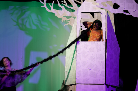 U of G student actor, ensemble, pulling the hair of Rapunzel (played by Meera Sontam) who is up in a decorative tower on stage in a production of "Into the Woods" at War Memorial Hall at the University of Guelph. The backdrop is set as a forest with trees. Photo credit: Joshua Lonuzzo