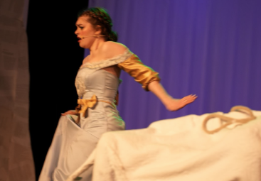 Georgia Rutter as Cinderella on stage near a decorative animal in a production of "Into the Woods" at War Memorial Hall at the University of Guelph. The stage is set as a forest with trees.