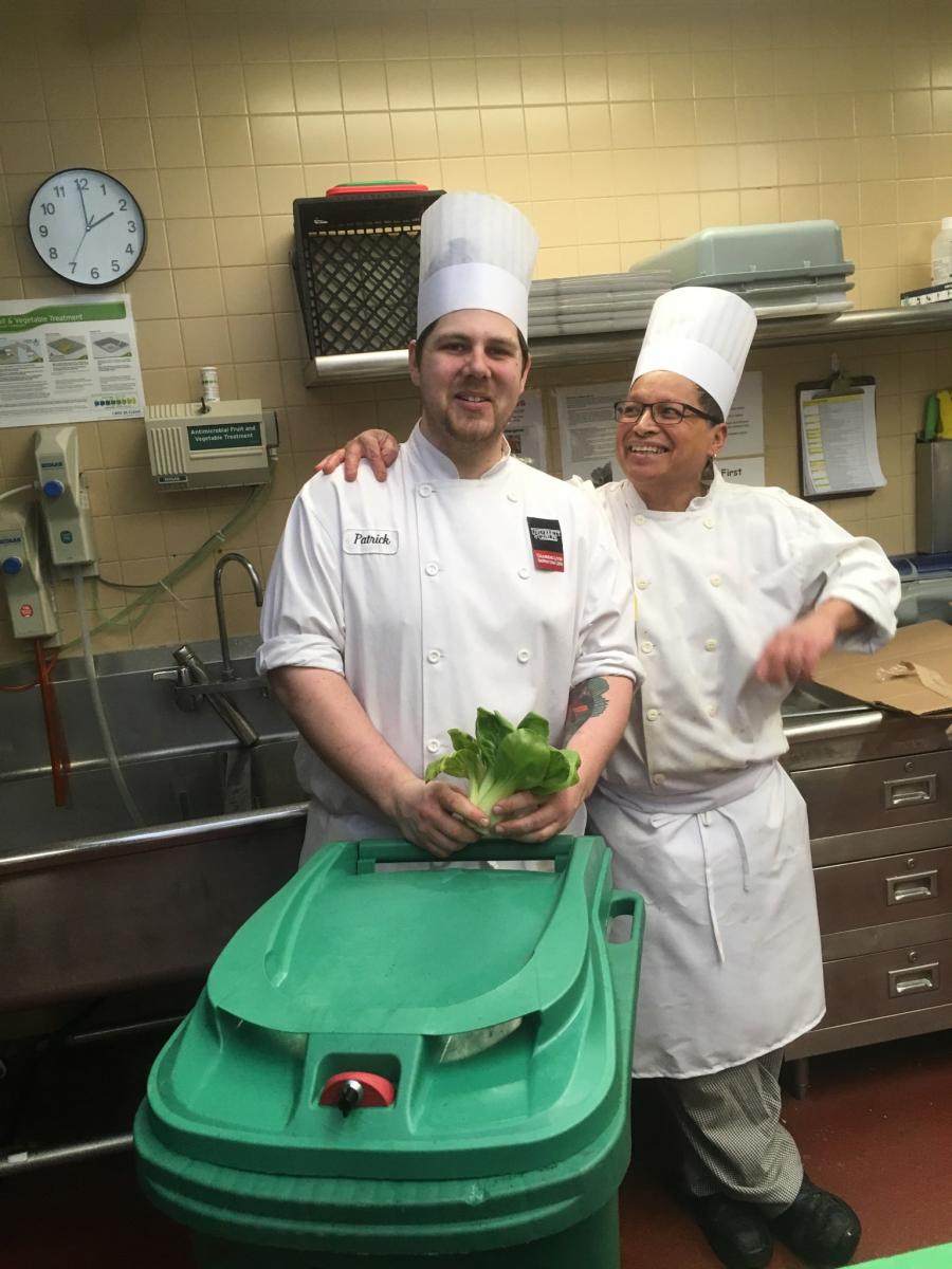 Two kitchen staff pose with a compost bin.