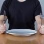 A person sitting at a dining table holding a knife and fork with a plate in between