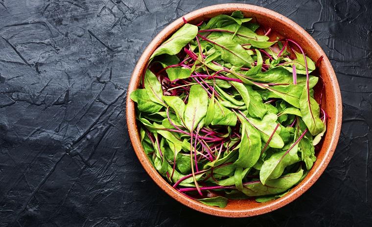 Bowl of leafy greens on a black table.