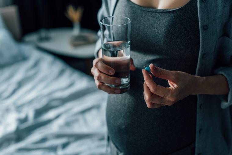 A pregnant woman holding a glass of water and a pill.