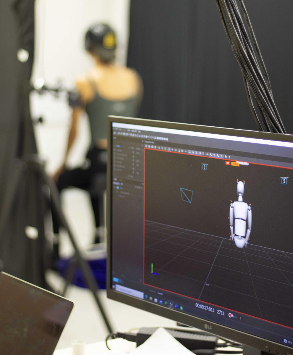 Computer screen shows model of a person, student sits in background wearing sensors