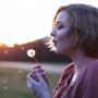 A women blowing a dandelion outside on a spring day