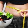 woman with measuring tape held around waist with bowl of veggies in her hand