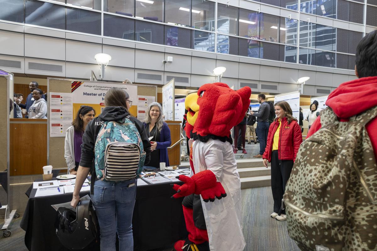 Gryph interacts with a group of staff and event attendees at the Grad Preview Day booth.