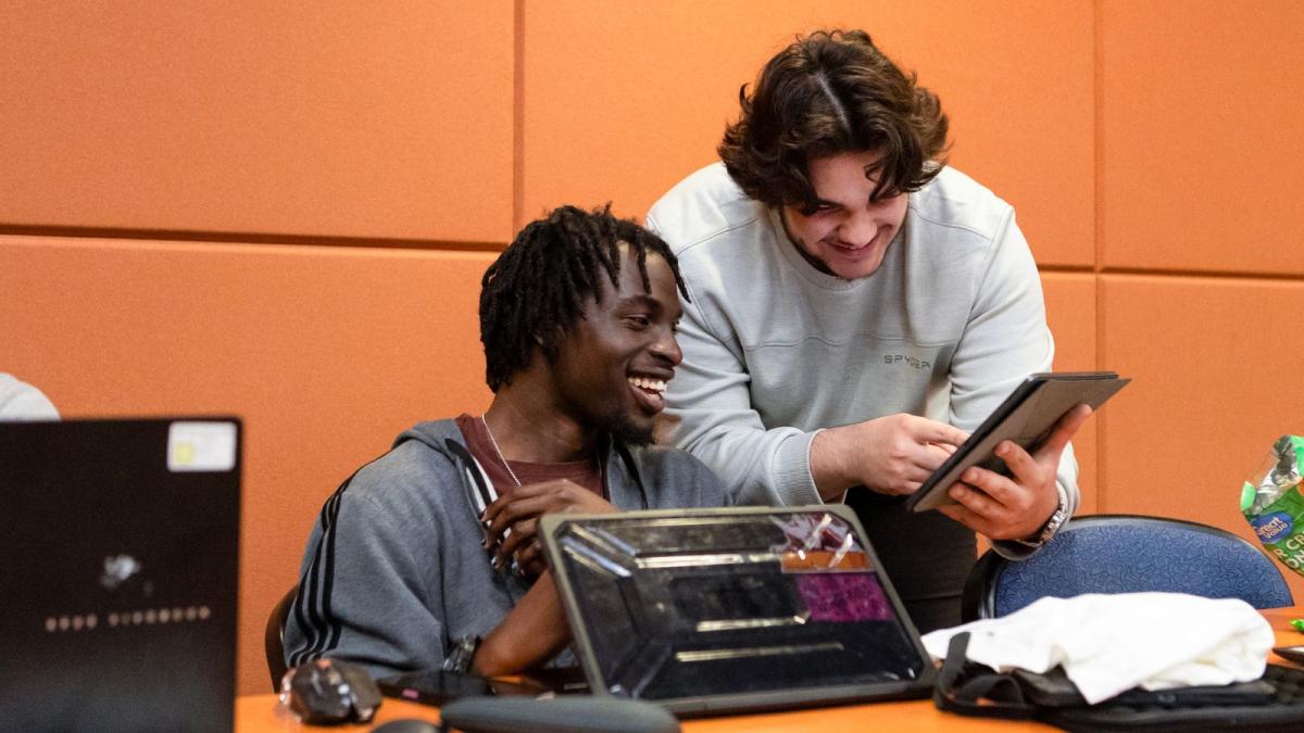 Two students looking at a tablet together and smiling.