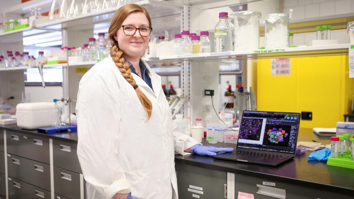 Megan Black posing with a computer in a chemistry lab.