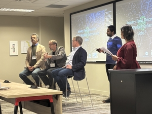 Three panelists sitting together with 2 people standing off to the side, leading discussion.