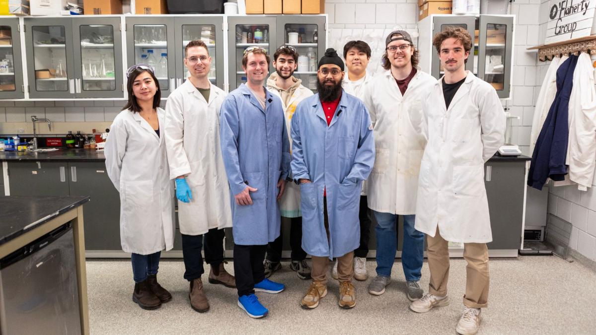 Eight people standing in a lab and smiling for a group photo.
