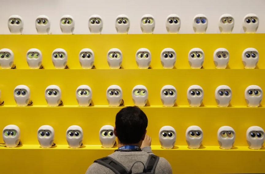 A person is standing in front of a yellow wall full of small robots.