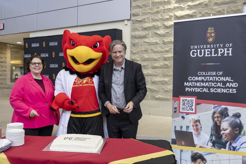 Interim dean Dr. Stacey Scott, Gryph and provost and vice-president academic Dr. Bill Rosehart at cake cutting ceremony for CCMPS. A cake is on a table in front of them, and a CCMPS roll-up banner is to the right.