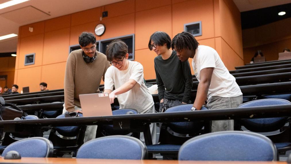 Four students standing around a laptop.