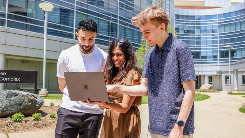 Dr. R. Ayesha Ali, Michael Czomko, and Aman Bhullar looking at a laptop and smiling.