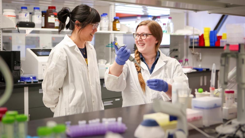 PhD candidate Megan Black and Dr. Rui Huang smiling at each other in a chemistry lab.