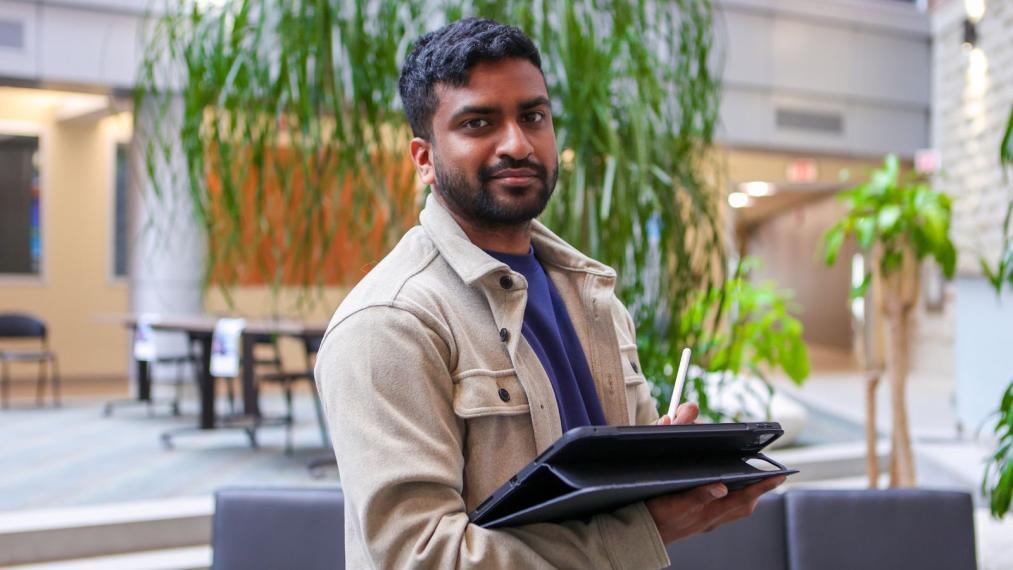 Kevin Pirabaharan, MCLC program, holding a tablet and standing while smiling at the camera.
