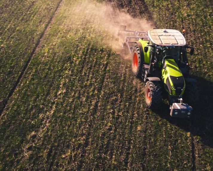 Tractor plowing through feilds blowing up dust. 