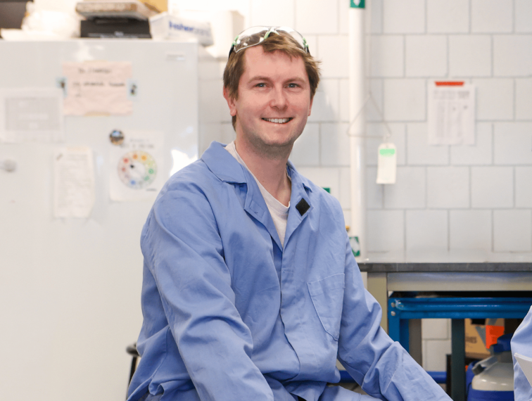 Dr. Derek O’Flaherty, Department of Chemistry, sitting in the lab and smiling at the camera.