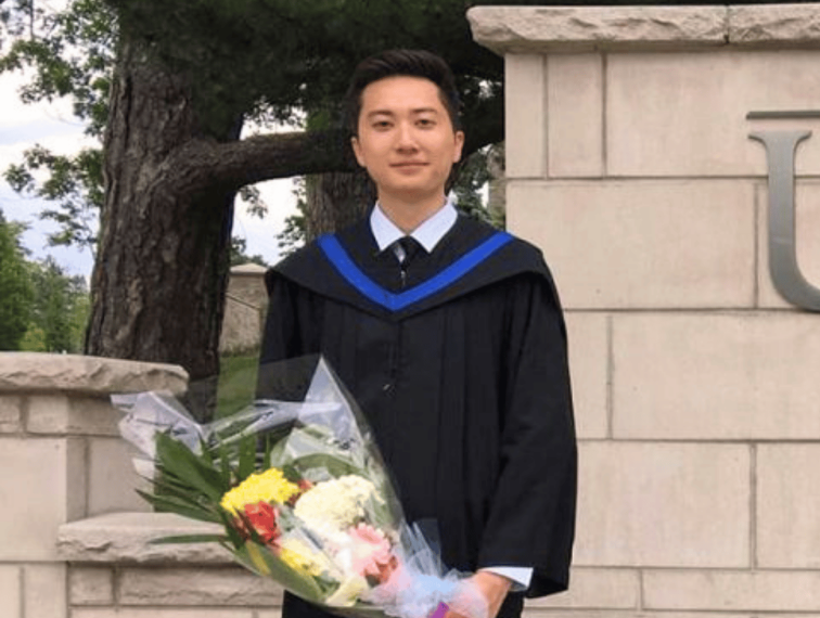 Dennis Kao in a graduation gown holding flowers.
