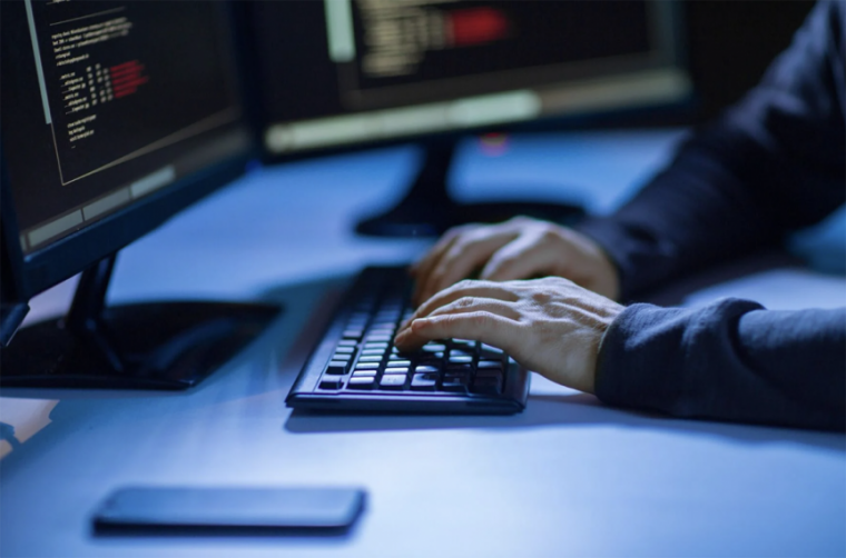 A person typing in a dark room with multiple monitors