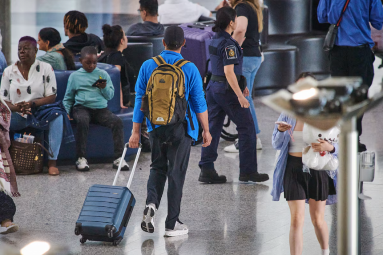 A traveller walks through a busy airport with a backpack and a suitcase