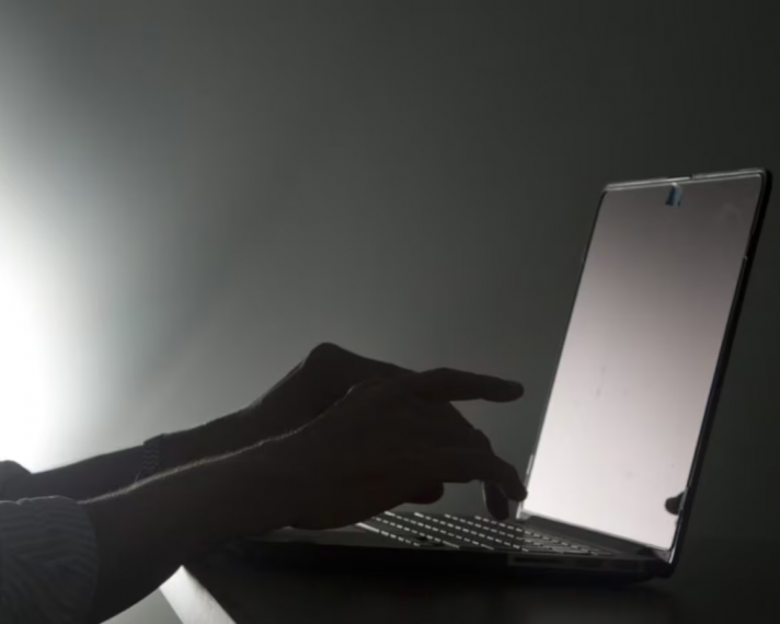 Hands typing on a laptop in a dark, black and white setting.