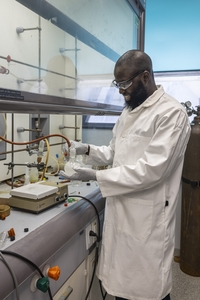  Mukaila A. Ibrahim wearing a lab coat and holding a beaker in a lab.
