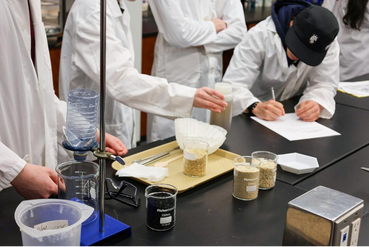 Several students in lab coats writing on a paper and examining a water engineering science lab.