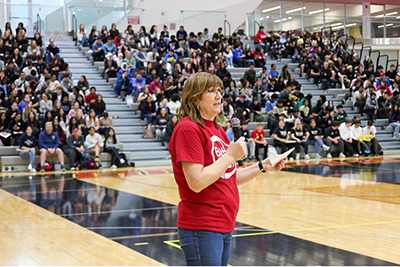 Bonnie Lasby announcing the challenge winners to a gymnasium full of students.
