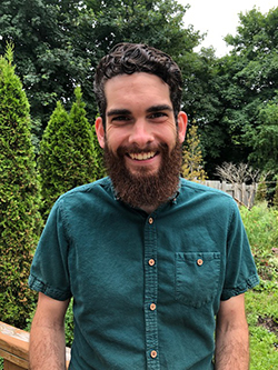 Department of Philosophy PhD student, Dylan White, smiling outside surrounded by greenery