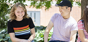 Two students laughing and enjoying each other's company outdoors on U of G campus during summertime.