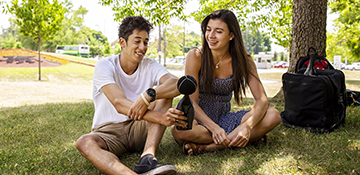 Two students sitting outside on U of G campus grass in the summertime while smiling and looking at environmental engineering equipment