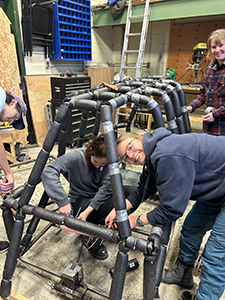 Two team members working on toboggan, one smiling at camera with glasses on