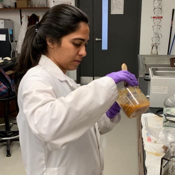 Student wearing a white lab coat working with material in a beaker.