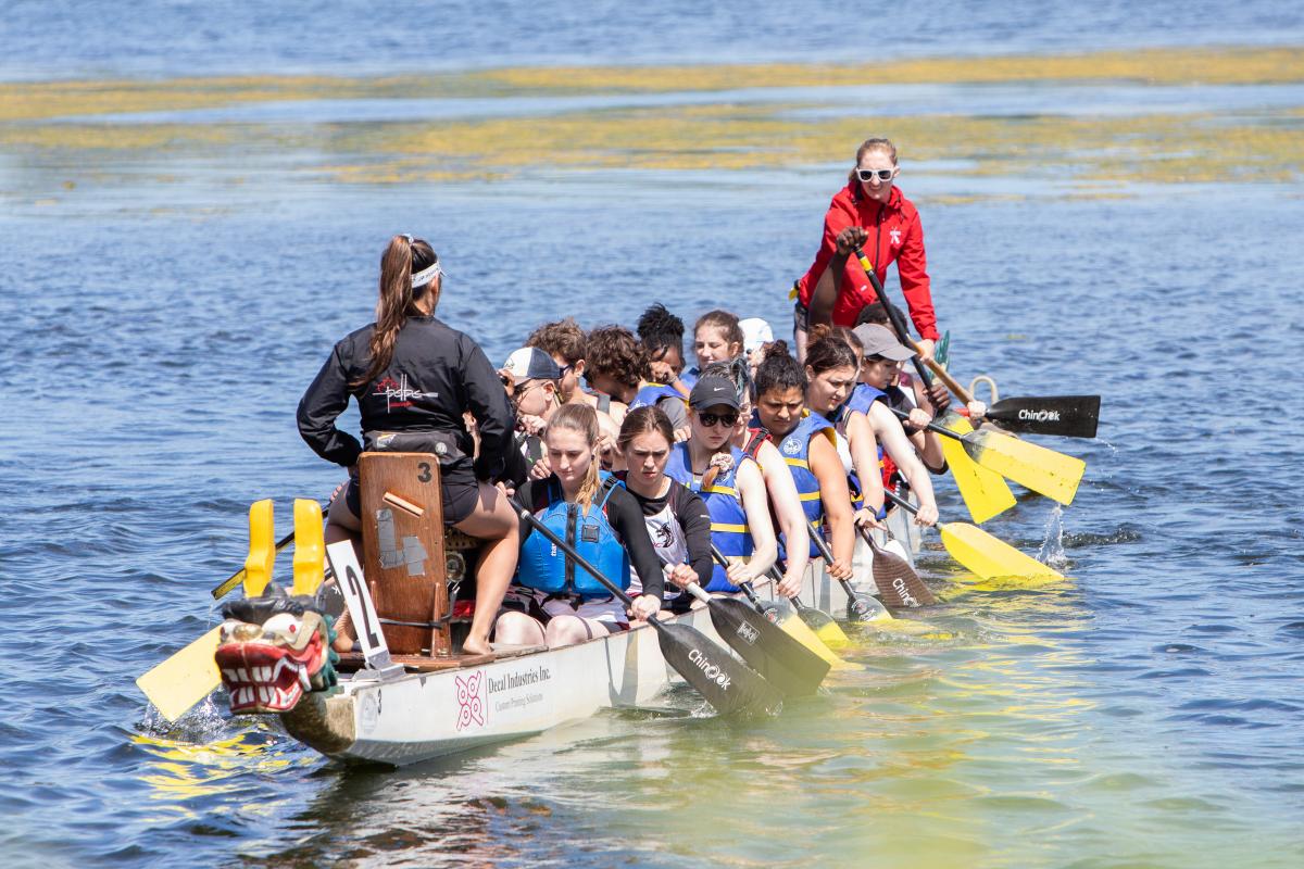 several people are rowing forward in a dragonboat while being instructed by two boat leaders