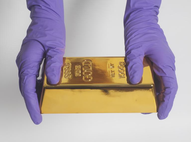 gloved hands holding gold bar