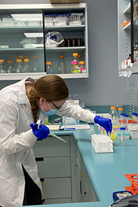 Jasmine working in a lab bent over some lab equipment and assessing a sample.