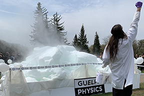 Orbax in front of a large steaming box in front of a crowd - the box has Guelph Physics on it 