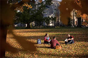 Students sitting on grass of Johnston Green during fall